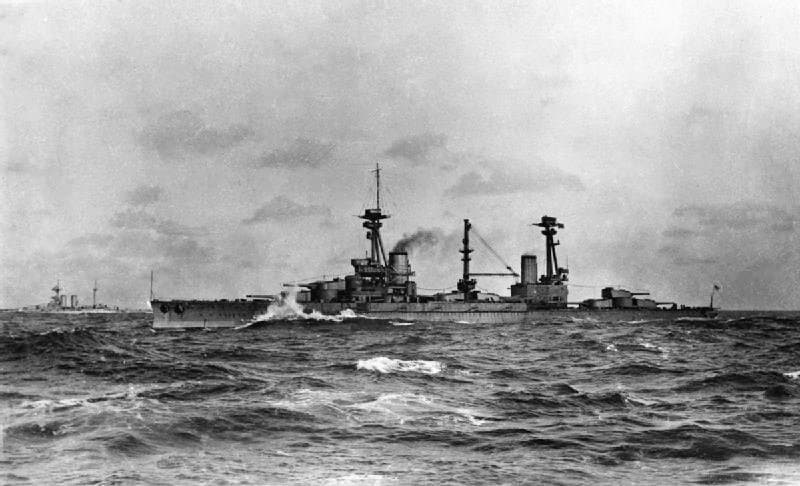 Naval vessels with guns and smoke coming out of one of its two turrets. The water is choppy. There is another ship in the distance. .