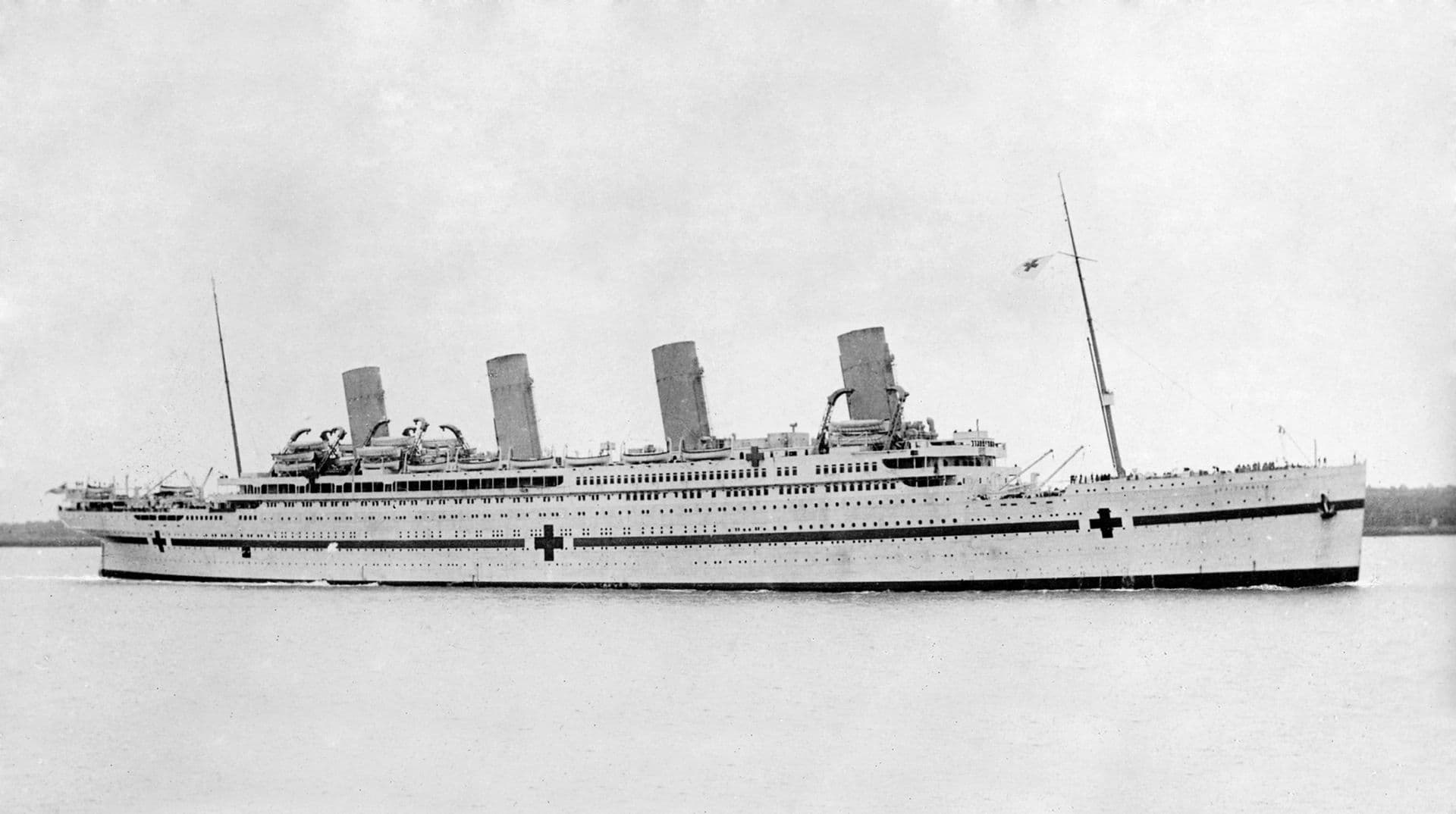 Large ship with multiple decks, 4 turrets and two masts. Large crosses are painted on the hull. People are on the deck and there are many lifeboats