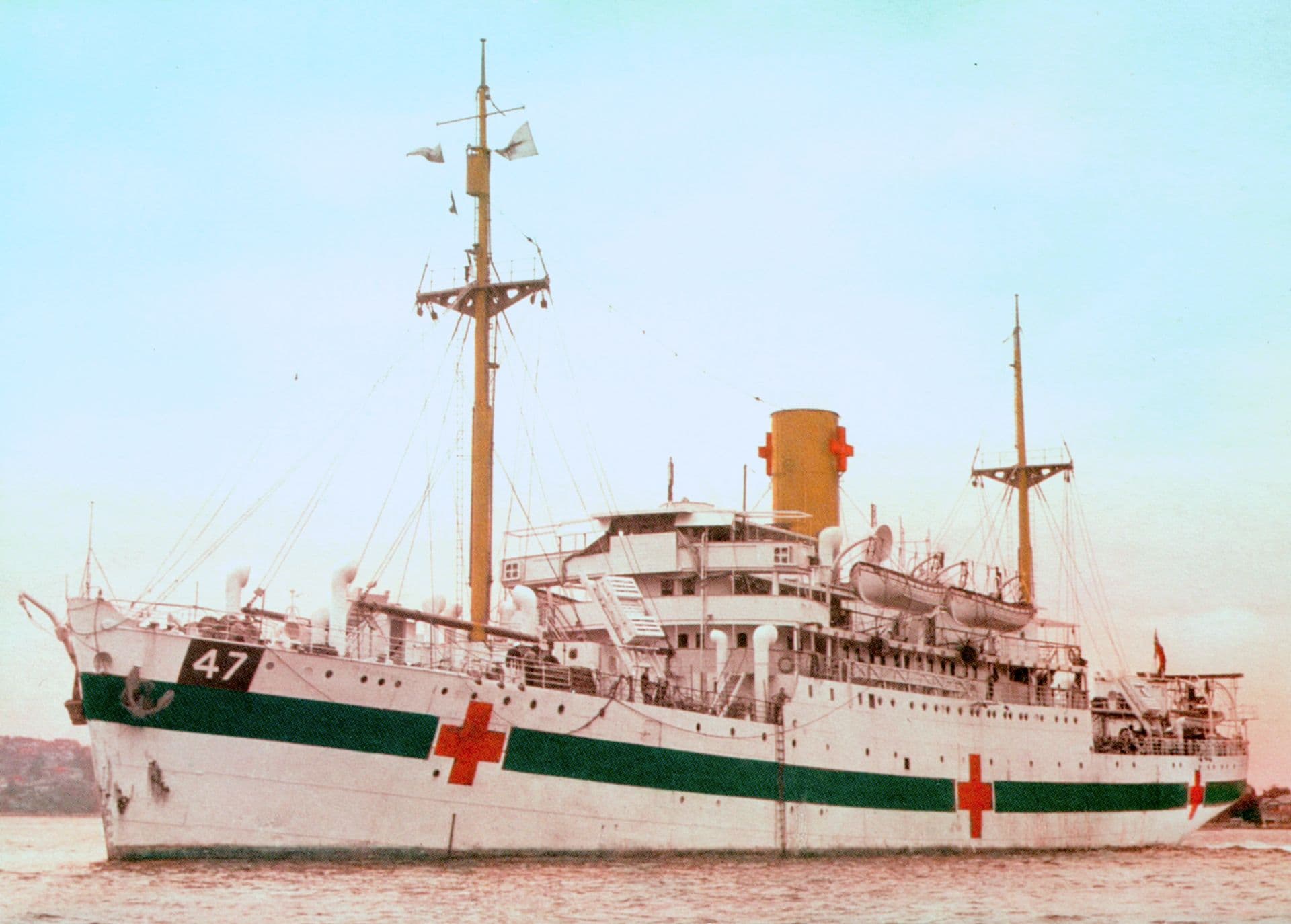 Large white ship with 2 large masts and a large funnel. Red crosses are painted on the hull of the ship and have been placed on the funnel.