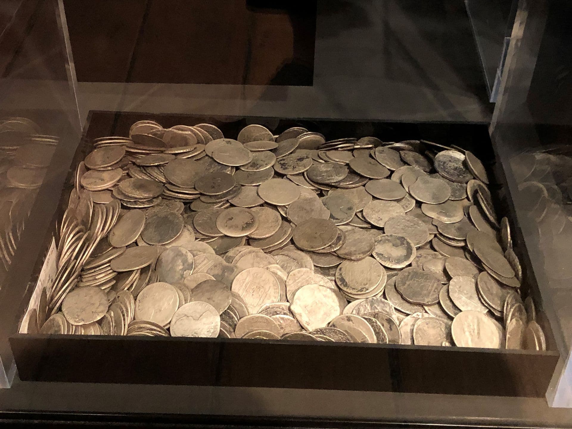 Photo of large number of silver coloured metal coins in a square container in a display cabinet.