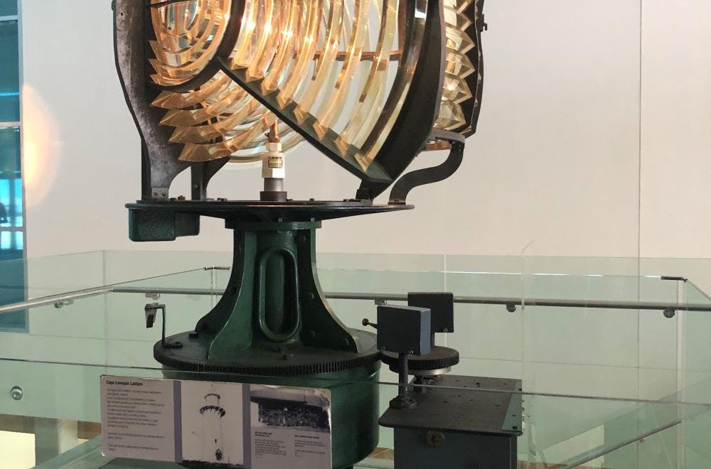 A large lighthouse lens mounted between the Museum stairs and elevator.