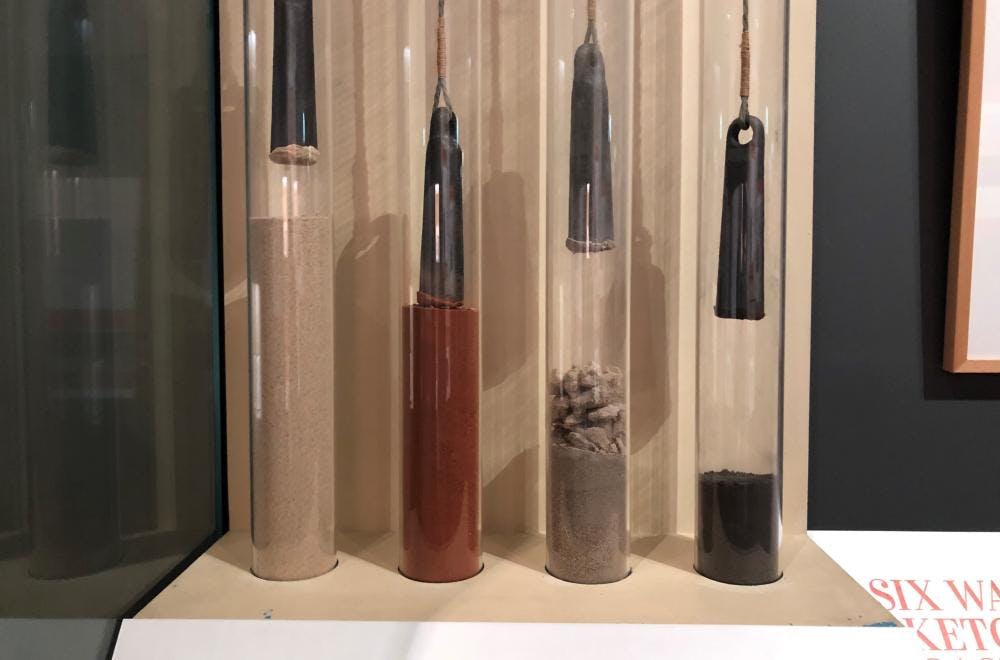 Cabinet containing four lead pieces suspended on string into glass containers with different samples of sea bed soils.