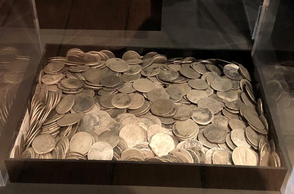 Photo of large number of silver coloured metal coins in a square container in a display cabinet.
