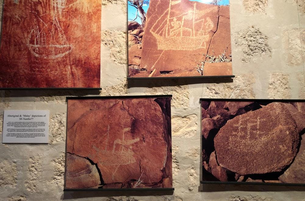 Photos of drawings of ships on red coloured rocks mounted on the wall of the gallery.