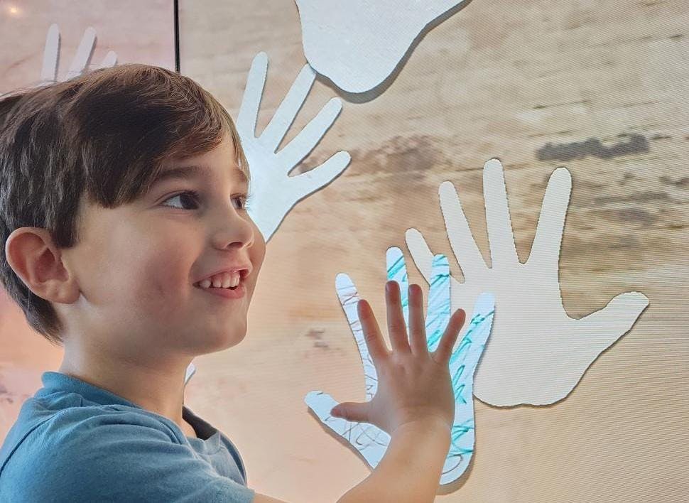 Young boy putting his hand up to an interactive screen 