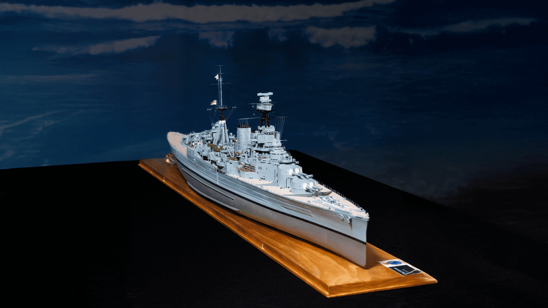Miniature model naval ship displayed on a wooden base with a dark background.