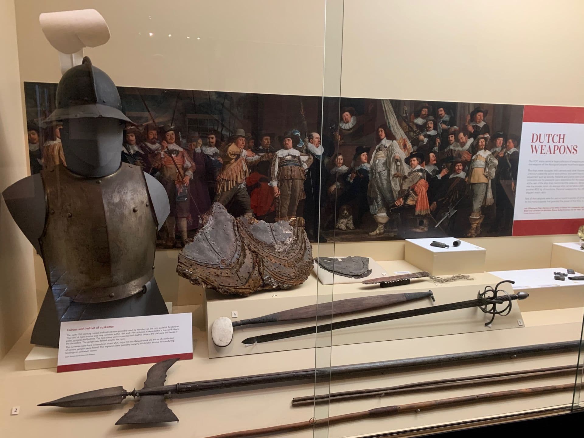 A glass fronted showcase, containing 17th century Dutch weapons such as a sword, armour and a pistol. These are contrasted with Aboriginal tools and weapons including a spear and spear thrower.