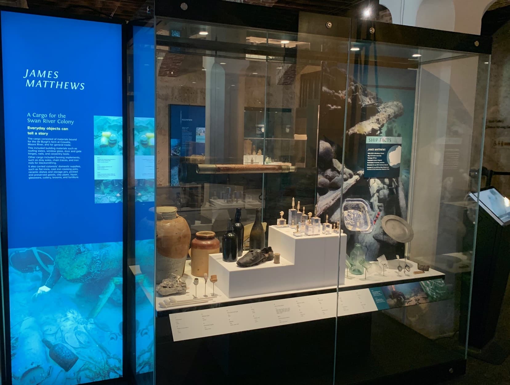 A glass cabinet containing items found from a shipwreck, including a leather shoe, an ivory chess set, glass bottles, and a china dish.