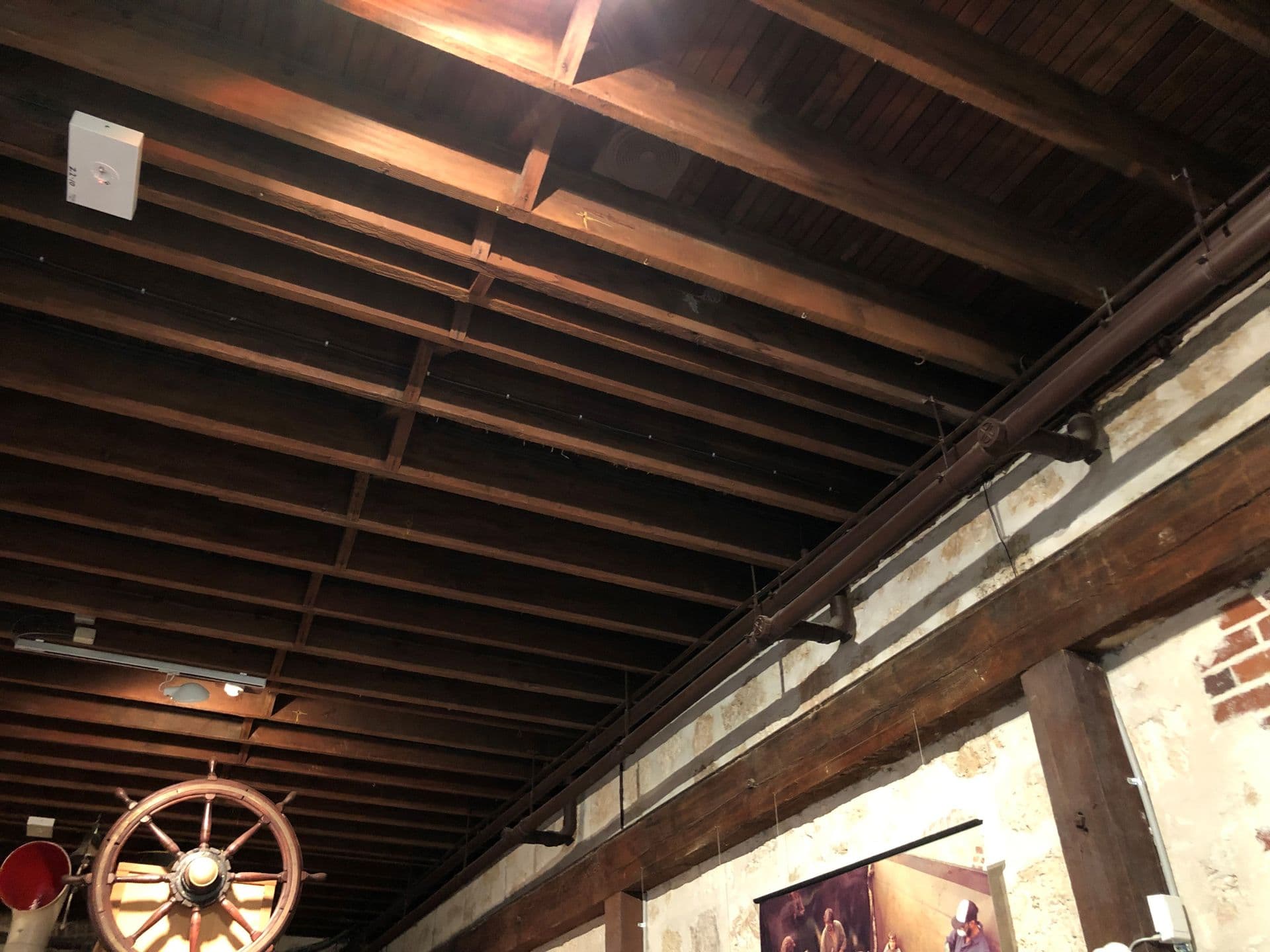 Dark brown wooden beams running across the ceiling of the gallery with stains and marks on them.