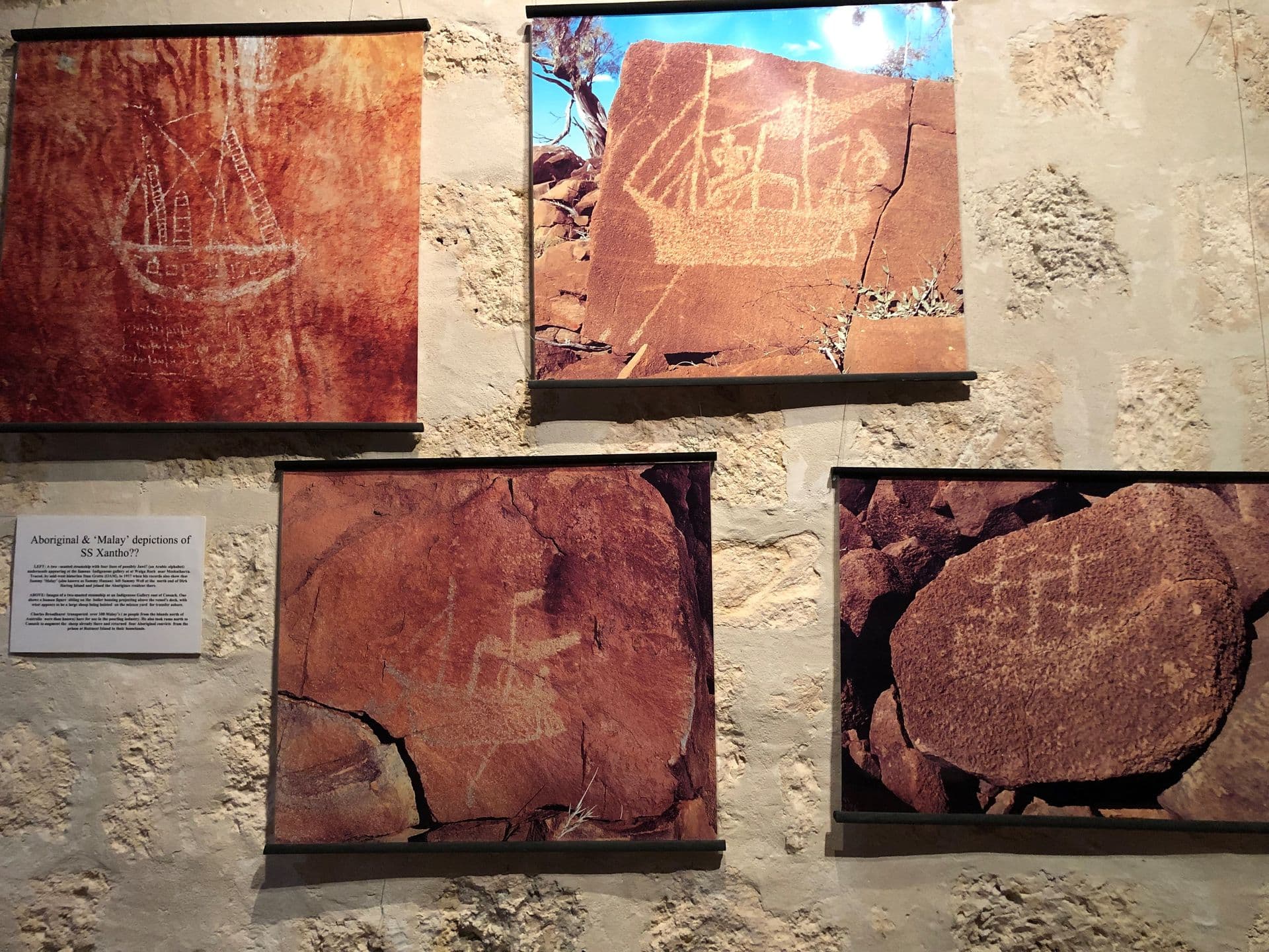 Photos of drawings of ships on red coloured rocks mounted on the wall of the gallery.