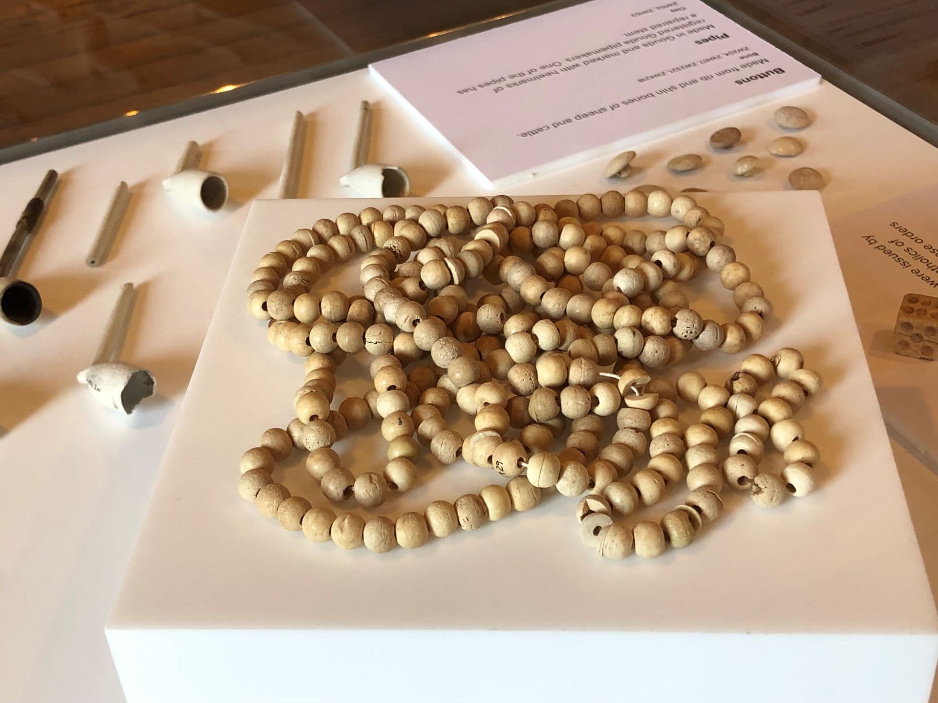 String of pale tan coloured wooden beads piled on a box in the display cabinet.