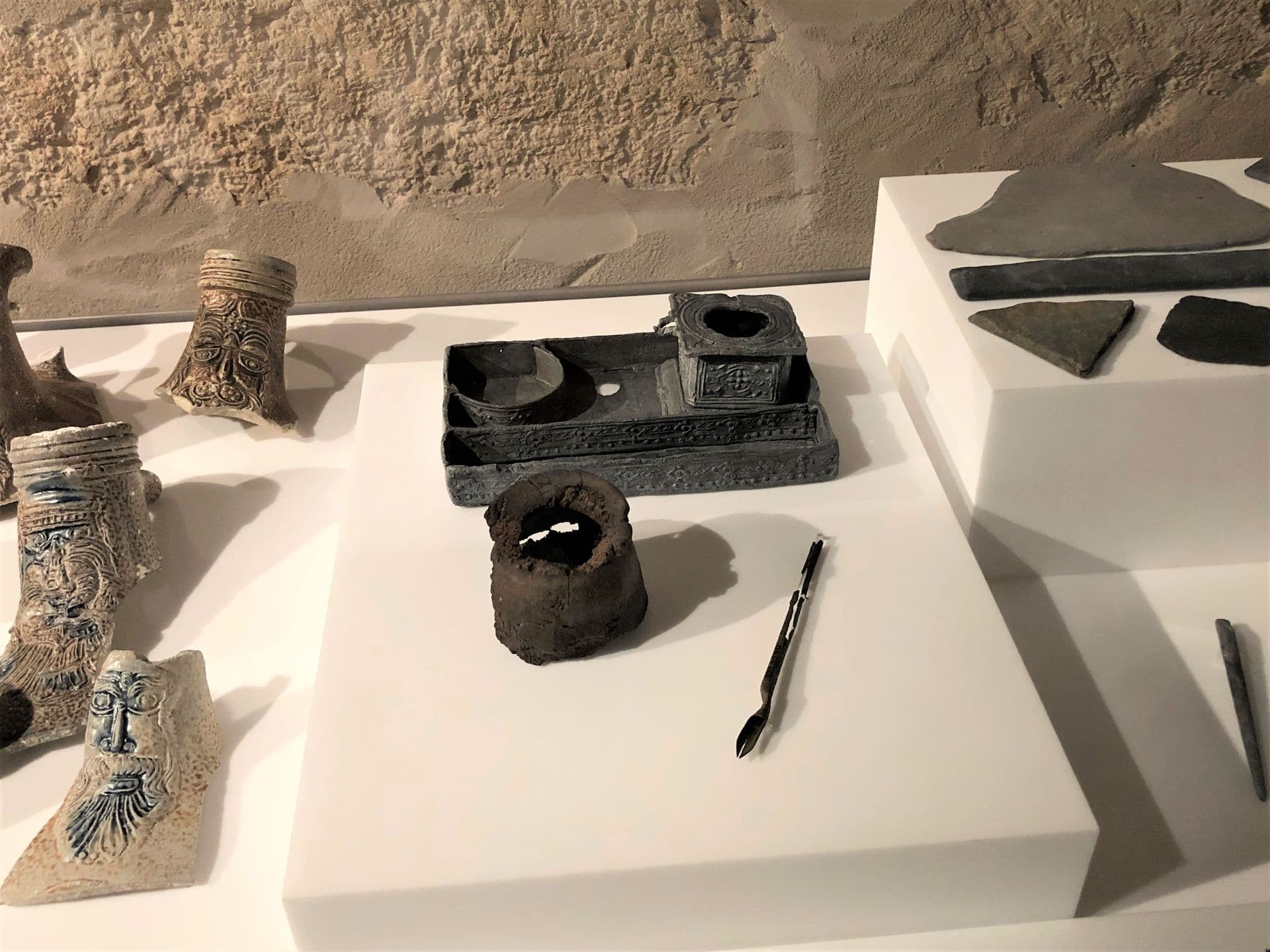 A decorated ink stand, a round wooden container that may be a pen holder, and a brass pen on display in the Museum.