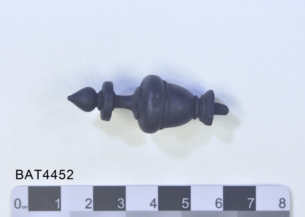 A black wooden chess piece in the Museum display cabinet. There is a small chip in the side of the piece.