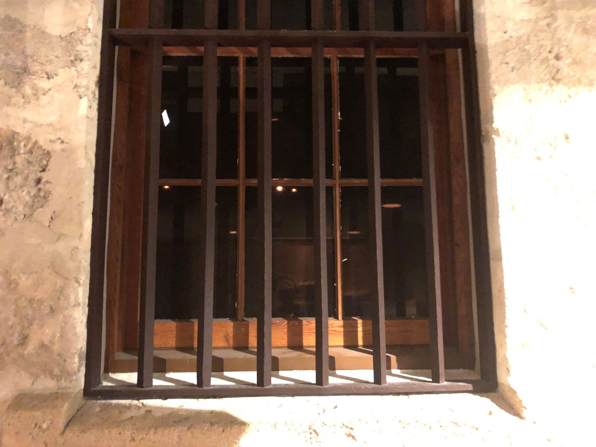 Square shaped vertical steel bars mounted in front of the wooden window frame.