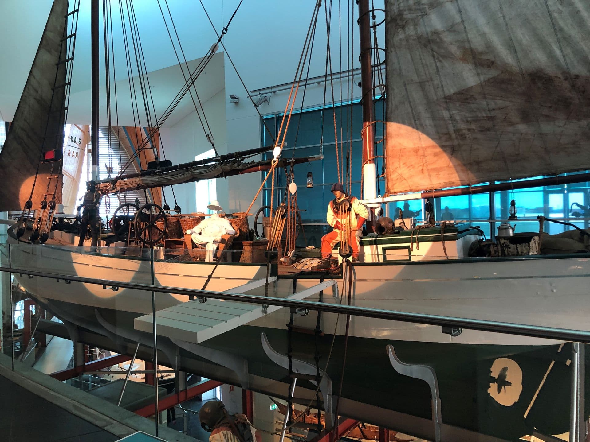 A large white and dark green sailing boat suspended next to the top floor. A mannequins in a diving suit sits on the deck.